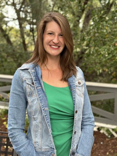 Allison Eckmann smiling outdoors, wearing a denim jacket over a green top.